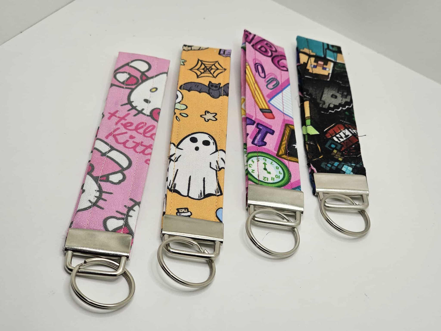Set of four handmade Halloween ghost-and-bat fabric wristlet keychains with colorful prints and metal rings.