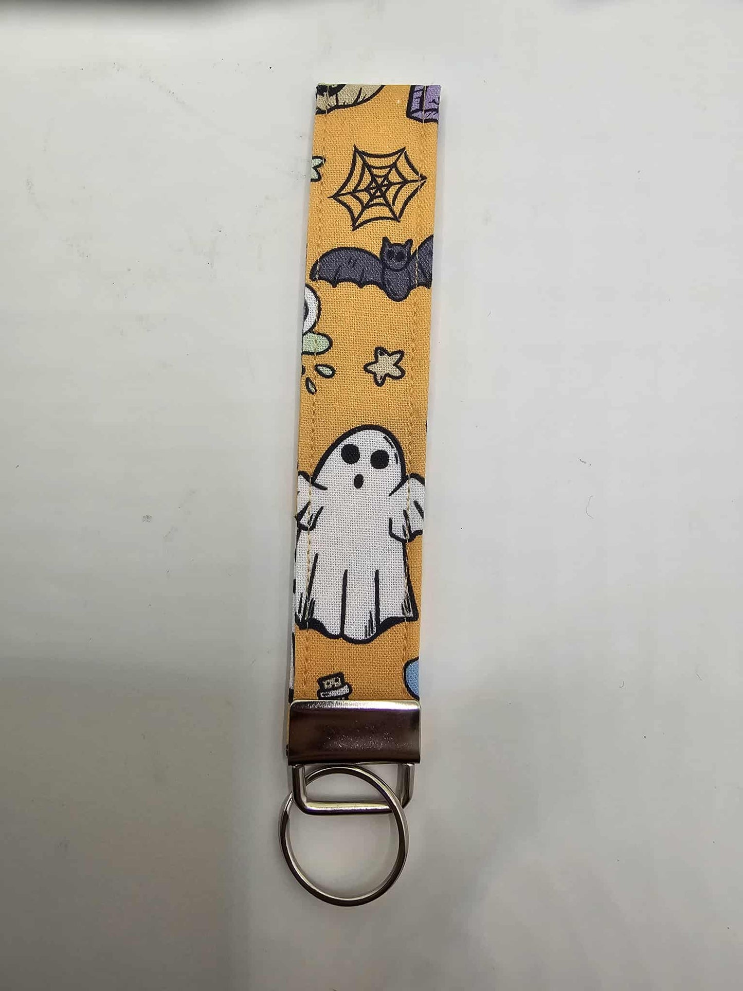 Halloween ghost & bat fabric wristlet key holder on orange backdrop with ghosts, bats, stars and spiderwebs.